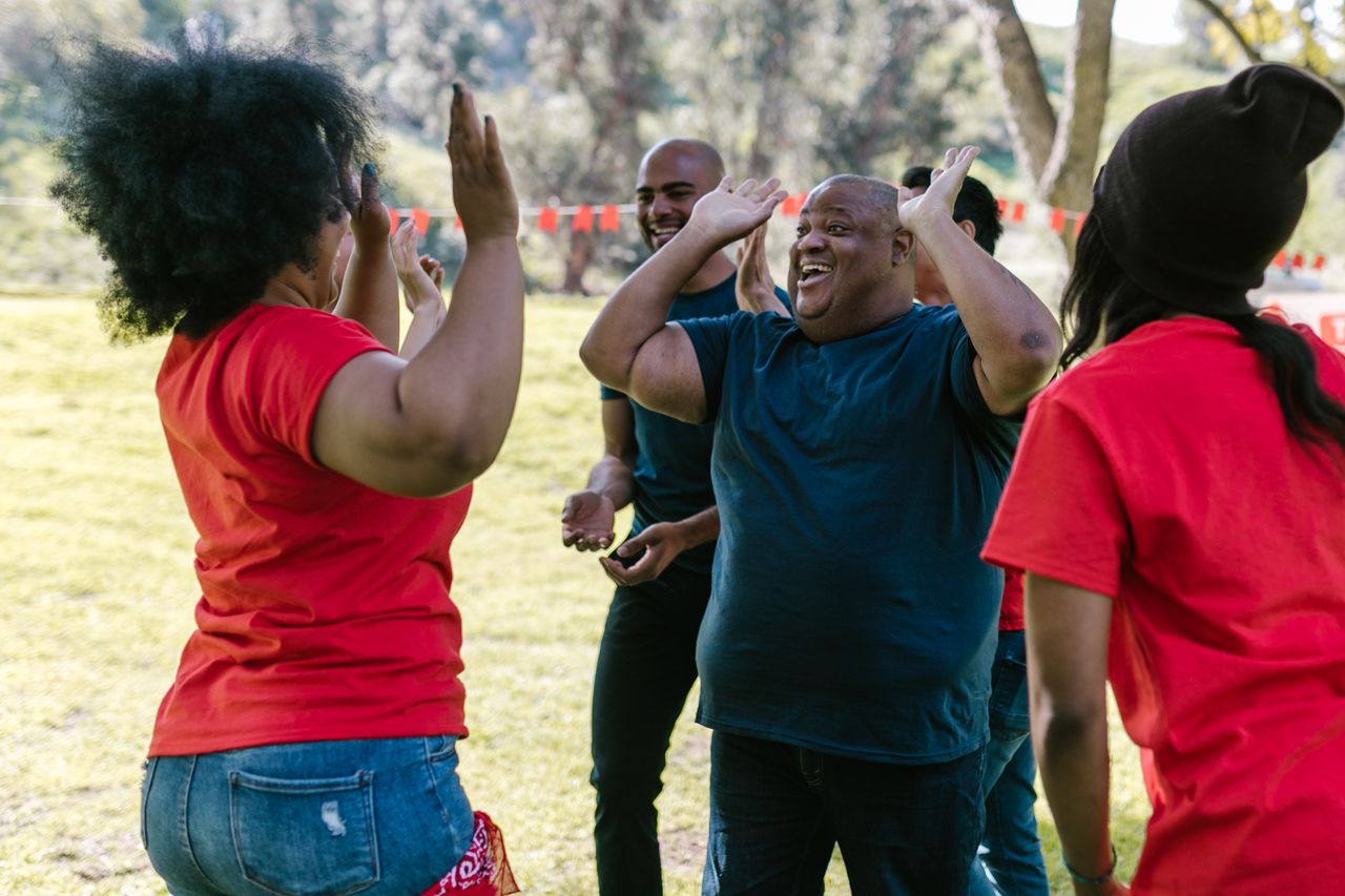 A joyful group of diverse adults high-fiving each other outdoors, showcasing team spirit.